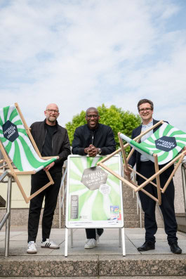 Moritz van Dülmen, Joe Chialo, Hannes Langbein are standing with branded chairs and a poster 