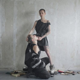 A man kneels in front of a woman who holds him by the hair and opens his mouth, both are dressed in clothes from FADE OUT LABEL