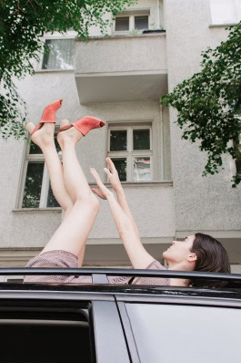 A woman is lying on the roof of a car with her arms and legs raised, wearing Maqu Shiringa Shoes 