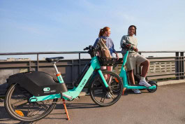 A man and a woman are standing on a bridge, and in front of them is a escooter and a ebike