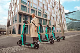 A woman stands next to several escooters in front of an apartment complex.