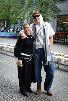 A couple poses in an embrace: the girl is dressed in a black jacket and black loose pants, and the guy is in jeans and a white jacket