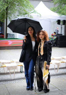 Two women posing: on the left holding an umbrella, dressed in jeans and a black jacket, on the right wearing loose dark gray jeans and a black blouse