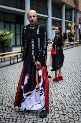A man posing in a long black and red skirt and black jacket