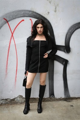 Drag queen poses in a short black dress and high black boots