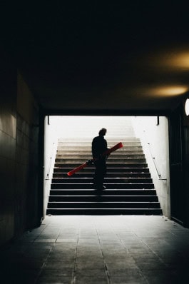 A man in sports equipment from Peak Performance Store Berlin with a snowboard in his hands stands in a darkened underpass 