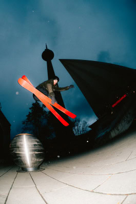 A man wearing sports equipment from Peak Performance Store Berlin performs ski tricks on the street 