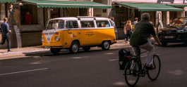 A man rides a bicycle along the road, with a yellow van standing in the background. 