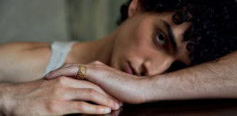 A man is lying down with a ring by Gina Melosi on his finger