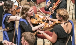 Two violinists smile at each other during their orchestral performance at the Young Euro Classic