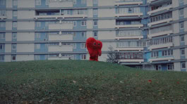 Still from the film Heart Rhythm where a large red heart stands in the middle of a clearing against the backdrop of a residential high-rise building
