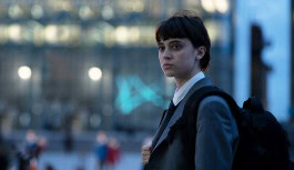 Still from the film Spirit of Ecstasy where a woman with a backpack on her shoulders and in a business suit stands on a city street