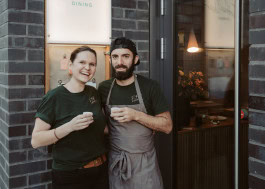 Two restaurant workers, a man and a woman, stand next to each other and smile