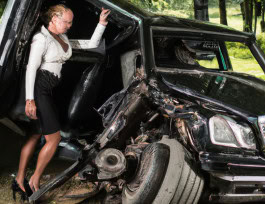 photo of a woman mannequin in an office suit holding the door of a car that was wrecked in an accident