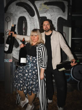 A man and a woman with large bottles of wine pose against a wall at the Blanc de Fck bar in Berlin 