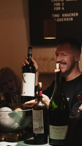 A bartender smiles and holds a bottle of wine behind the bar at Blanc de Fck bar in Berlin 