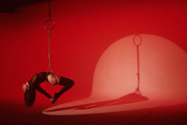 Shibari tied woman hanging suspended by hook in spotlight on red background in Shibari Studio Berlin