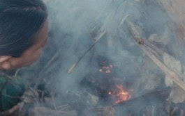 A woman blows on a smoldering fire full of smoke