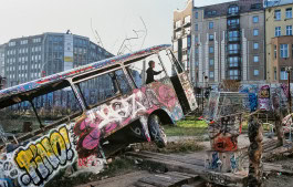 A little boy inside an abandoned graffiti-covered bus with residential buildings in the background