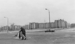 Man holding kite against abandoned car and grey residential buildings
