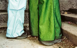 Feet in the shoes of two people standing opposite each other, one in pale blue wide pants, the other in green wide pants