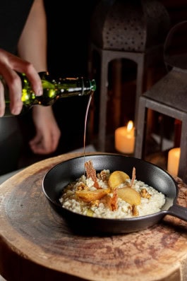 Man pouring oil over pumpkin risotto in frying pan on table