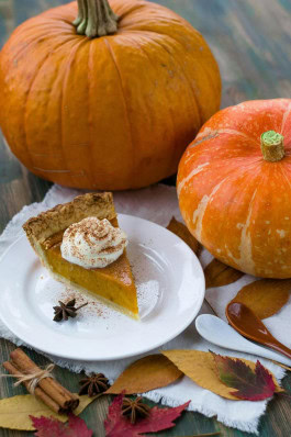 A piece of pumpkin pie on a plate next to pumpkins and autumn leaves