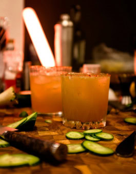 Two glasses of Pumpkin Margaritas on the table, with a sliced ​​cucumber around them