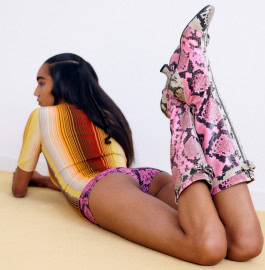 Girl with long black hair lying on her stomach with her legs up wearing an orange and white vertical striped t-shirt, purple zebra print short shorts and pink and white zebra print boots 