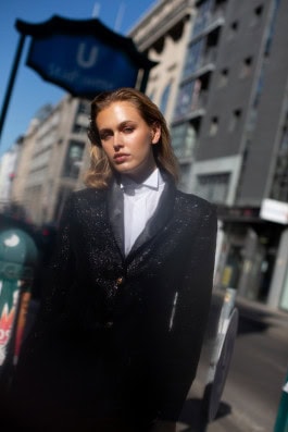 Girl with slicked back hair on street in shiny black suit and white shirt