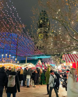 Berlin Christmas Market, crowds stroll between decorated Christmas stalls and garlands hanging overhead 
