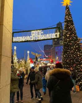 Berlin Christmas Market, crowds strolling between decorated trees, illuminated sign 