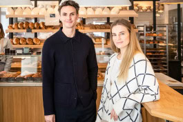 A man and a woman pose in front of a display of baked goods at the FREA restaurant
