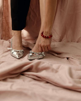 On pastel pink fabrics, women's legs in silver shoes and black trousers, a hand with a bracelet of amber stones hanging down 