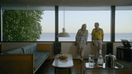 Still from the film Ragnar Kjartansson, where a man and woman talk while leaning on a windowsill in a house overlooking the ocean