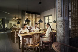 Two women and a man chat cheerfully in white coats while sitting at a table in a restaurant in Vabali Spa