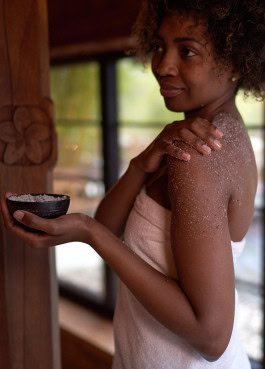 A woman in a white towel rubs a scrub onto her body that she holds in her hands at Vabali Spa 