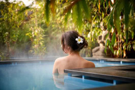 A woman stands with her back to nature in a hot pool at Vabali Spa, with a flower in her hair