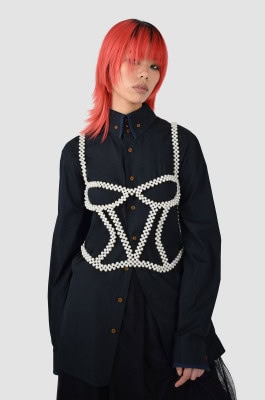 Peach haired girl in black pants, transparent black skirt, long black shirt and corset with pearls on top 