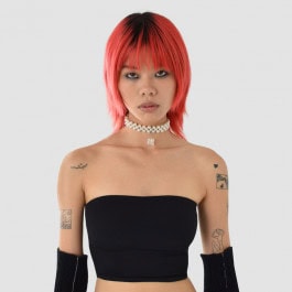 Girl with peach hair and tattoo in black top and black gloves with pearl choker