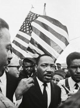 Camera Work exhibit, black and white photo of Martin Luther King Jr. making his way through a crowd of journalists, an American flag fluttering behind him