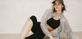 woman reclining on her side in black leggings, top, translucent blouse and cap 