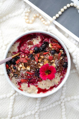 A bowl of oatmeal with blueberries, seeds, nuts and jam