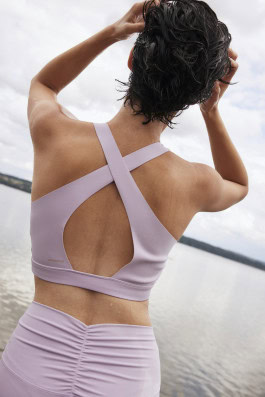 woman posing on pier with back in purple sports top and leggings 